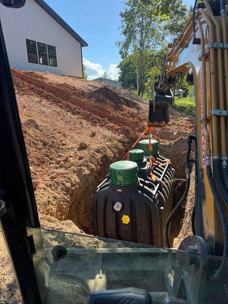 Excavator setting a new septic tank in an open trench